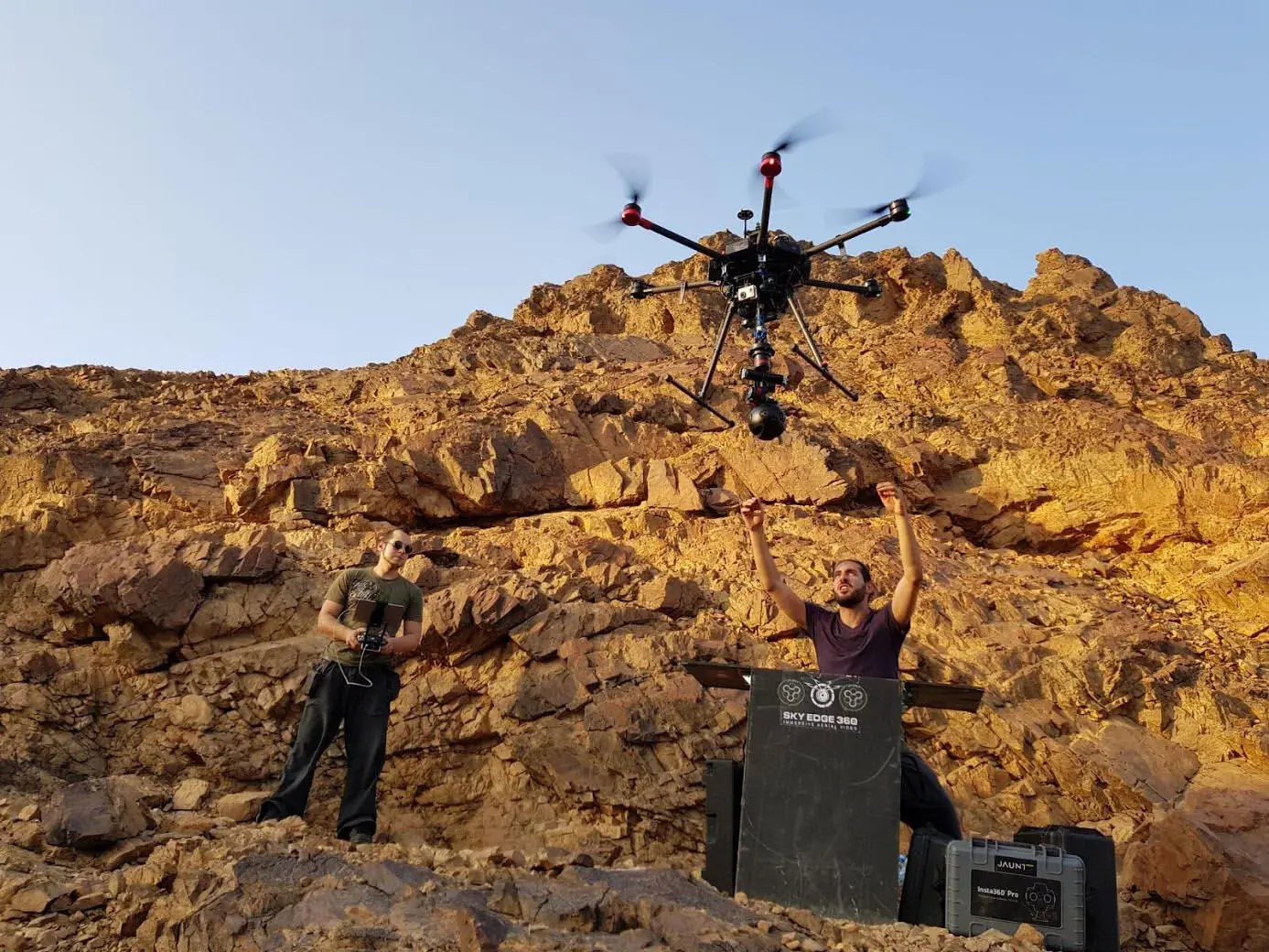 A 360 camera drone lifting off over red rock on the Red Sea coast, with the crew and ground rig below