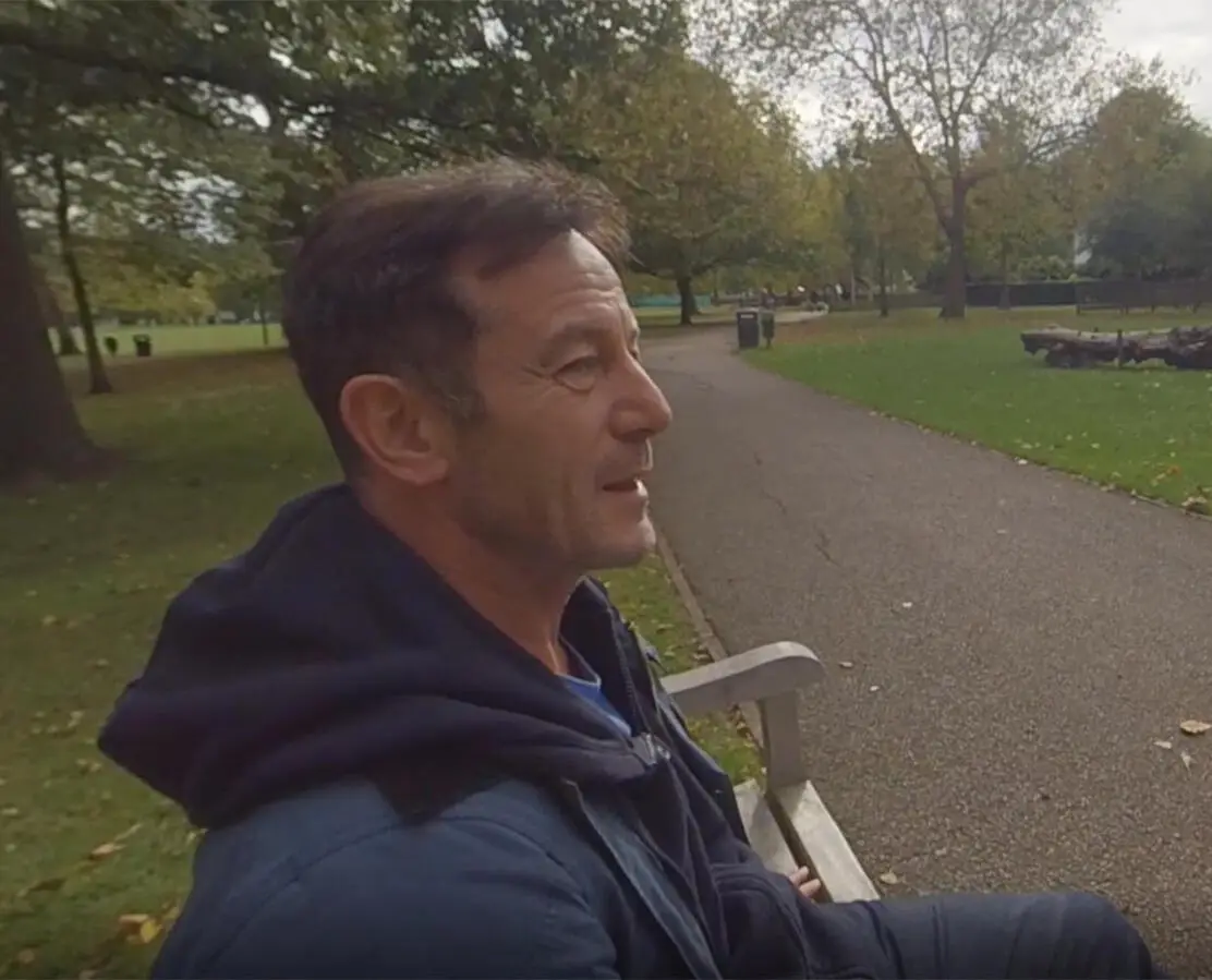 A man sitting on a park bench beside a path, in a frame from one of the mindfulness films